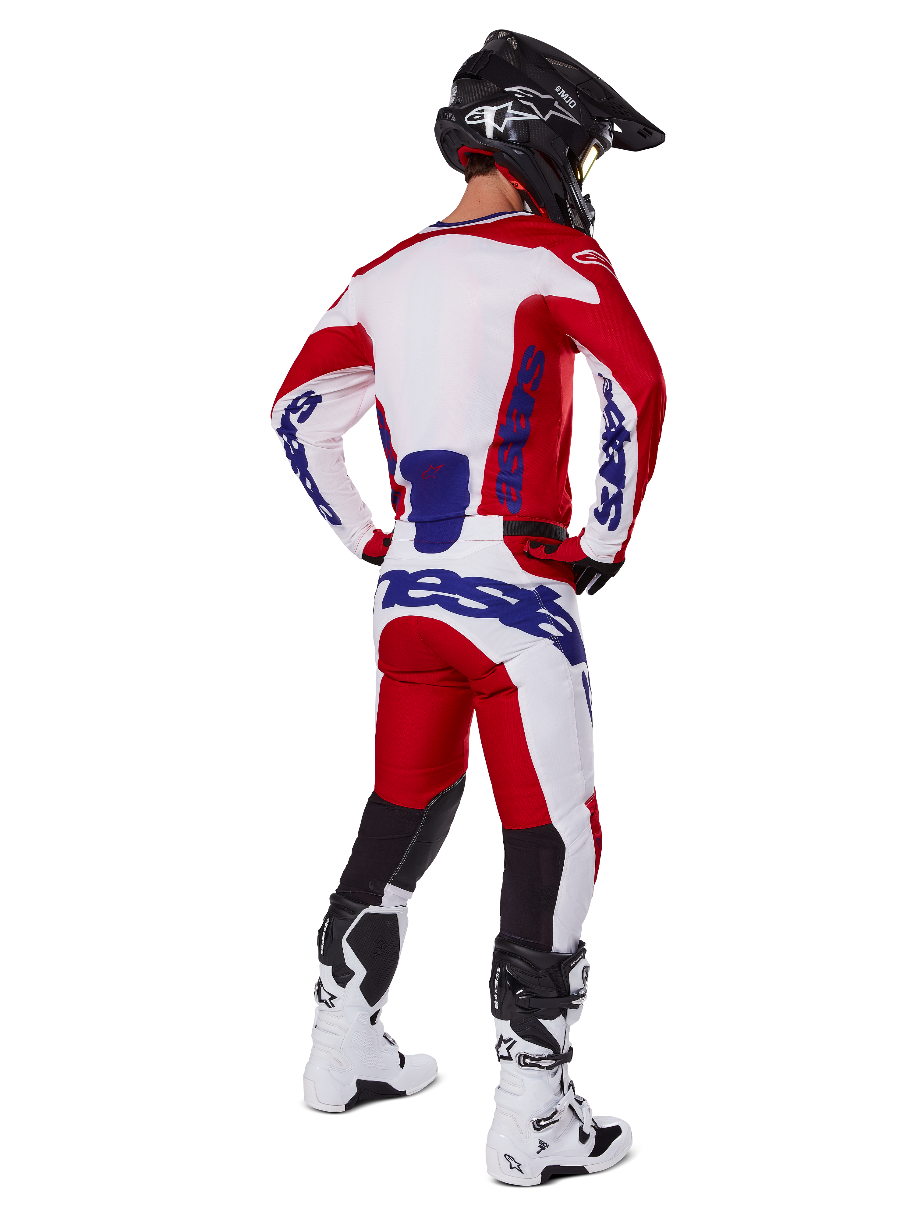 Alpinestars 2025 Racer Veil Pants, calças de motocross, vermelho vivo e branco com detalhes em azul, vistas de trás num piloto com equipamento completo, com o logótipo Alpinestars em destaque, painéis respiráveis na parte inferior das pernas, botas brancas e capacete preto coordenados