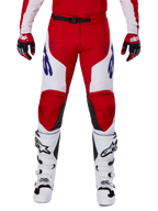 Alpinestars 2025 Racer Veil Pants, calças de motocross, vermelho vivo e branco, usadas com luvas vermelhas e botas brancas a condizer, com logótipos azuis nas coxas e um cinto preto na cintura, corte desportivo ergonómico para uma condução de performance