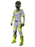 Calças Alpinestars 2025 Racer Veil, calças de motocross, cinzento e amarelo néon, usadas com camisola a condizer, capacete preto, óculos de proteção amarelo néon, botas e luvas, num conjunto de competição todo-o-terreno coordenado com design ergonómico e logótipos em destaque.