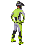 Alpinestars 2025 Racer Veil Pants, calças de motocross, cinzentas e amarelo fluorescente, vista traseira de piloto com equipamento completo, camisola a condizer e botas amarelo néon, com logótipos pretos destacados, kit técnico de corrida para todo-o-terreno