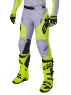 Alpinestars 2025 Racer Veil Pants, calças de motocross, cinzento e amarelo néon fluo, com logótipos de estrela pretos e cinto de cintura ajustável, apresentadas com botas e luvas de motocross a combinar, design ergonómico para condução todo-o-terreno