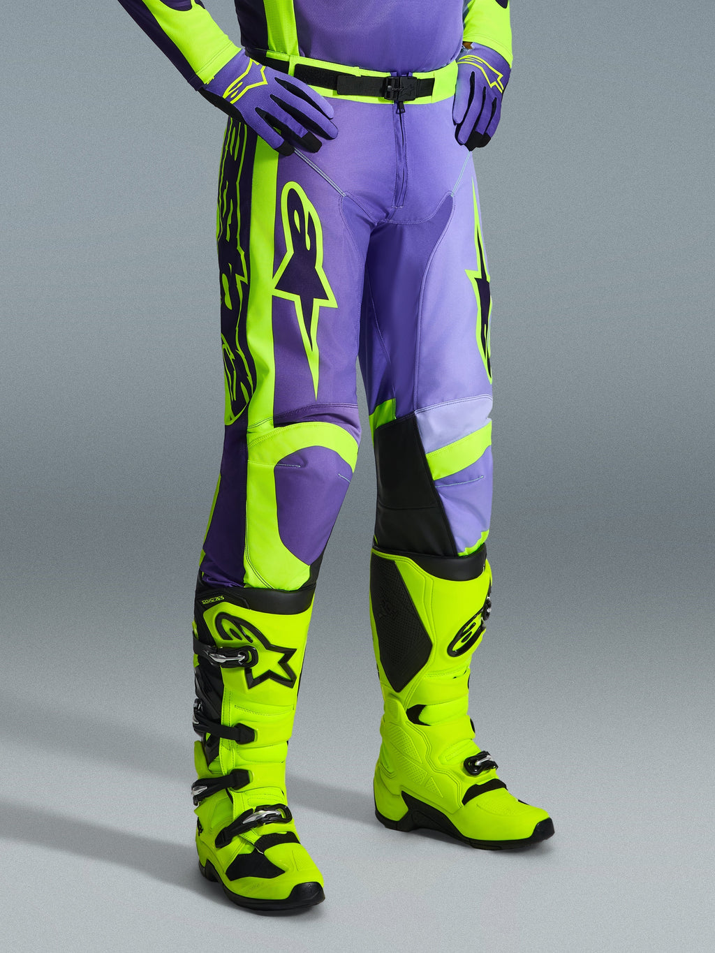 Alpinestars 2026 Racer Portl Pants, calças de motocross em roxo e amarelo néon, usadas por um piloto com botas amarelo néon a condizer e luvas roxas, com a marca Alpinestars em destaque e design ergonómico para performance off-road