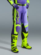 Alpinestars 2026 Racer Portl Pants, calças de motocross em roxo e amarelo néon, usadas por um piloto com botas amarelo néon a condizer e luvas roxas, com a marca Alpinestars em destaque e design ergonómico para performance off-road