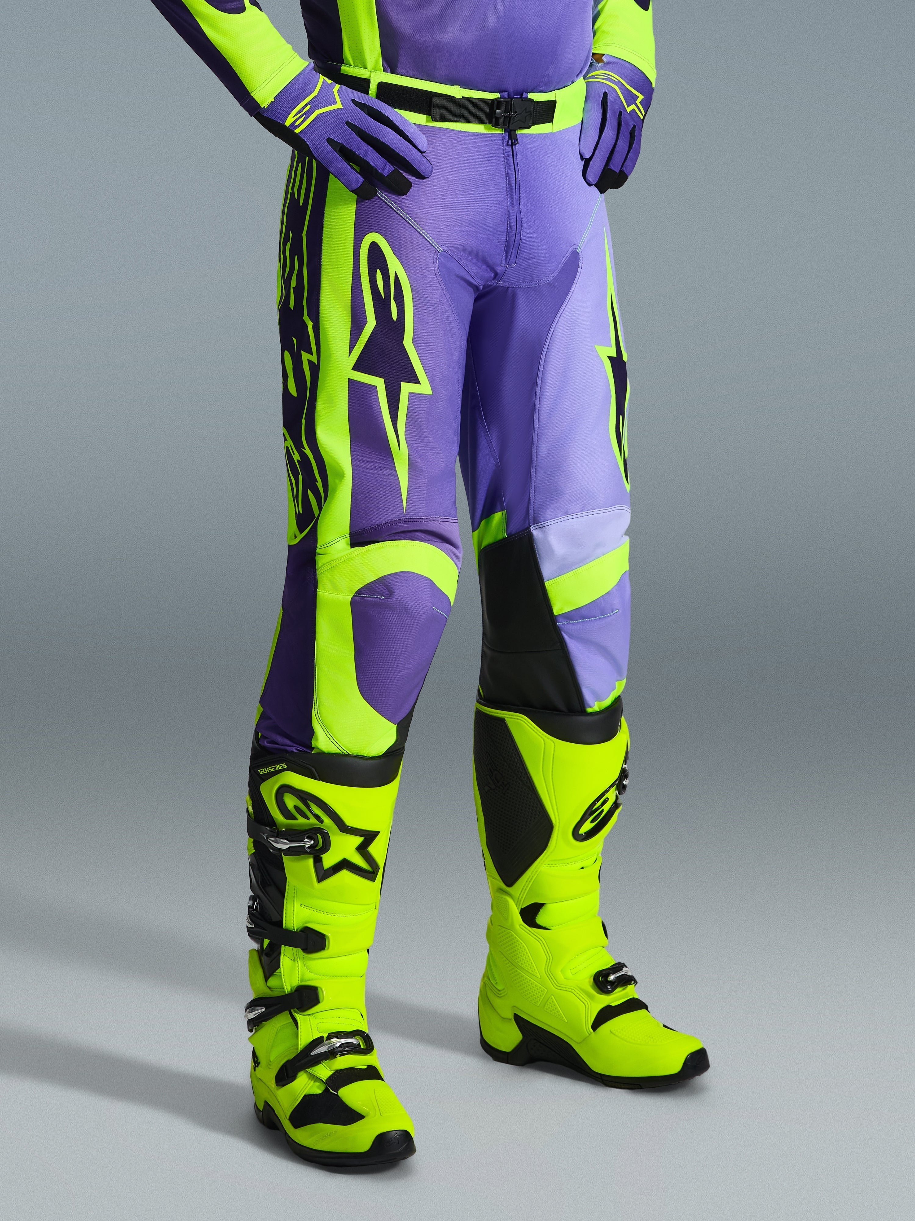 Alpinestars 2026 Racer Portl Pants, calças de motocross em roxo e amarelo néon, usadas por um piloto com botas amarelo néon a condizer e luvas roxas, com a marca Alpinestars em destaque e design ergonómico para performance off-road