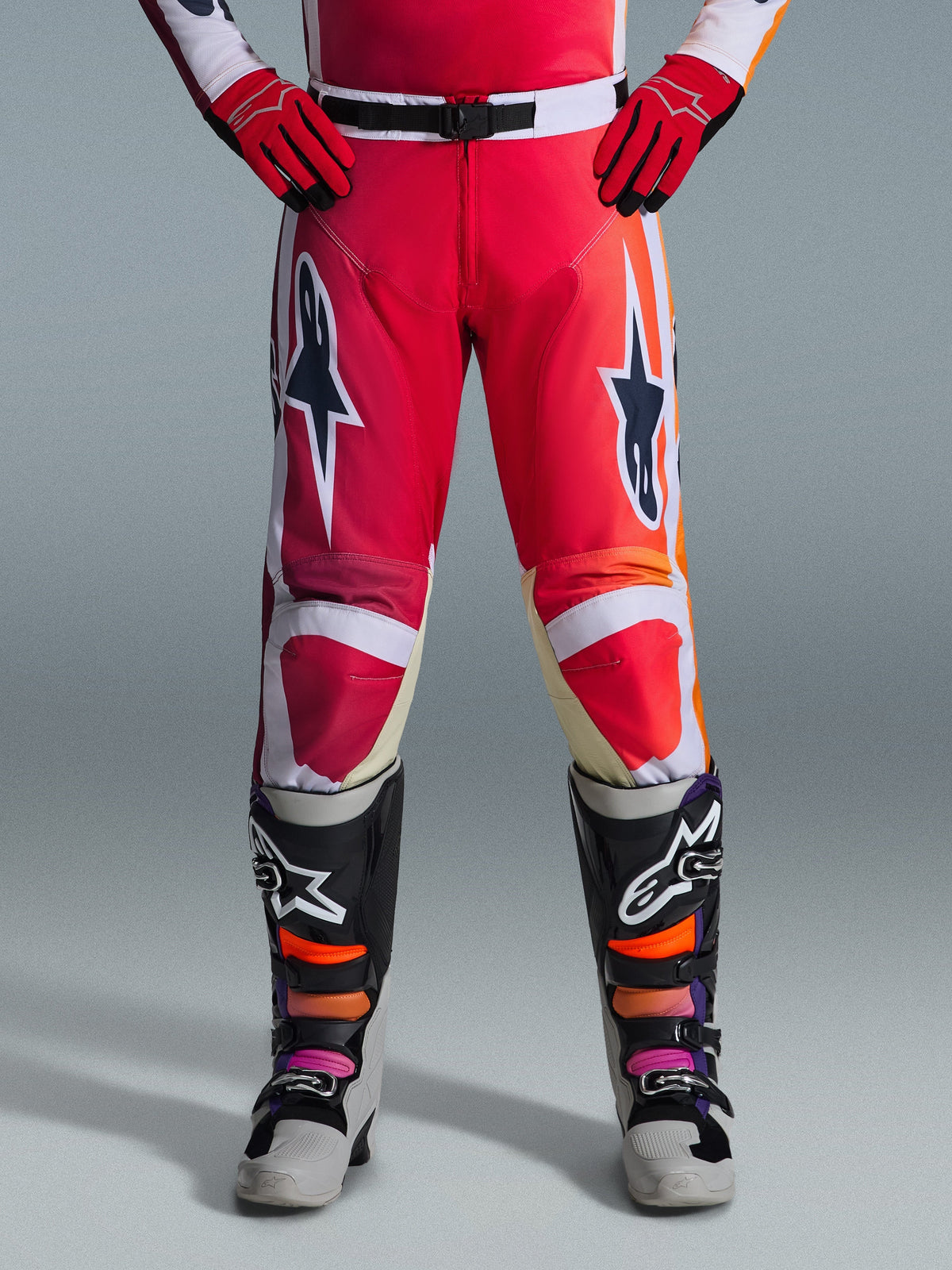 Alpinestars 2026 Racer Portl Pants, calças de motocross, vermelho, cinzento claro e cinzento escuro, usadas com luvas vermelhas a condizer e botas multicor, com logótipos de estrela Alpinestars destacados nas coxas e detalhes brancos, design desportivo para corridas off-road