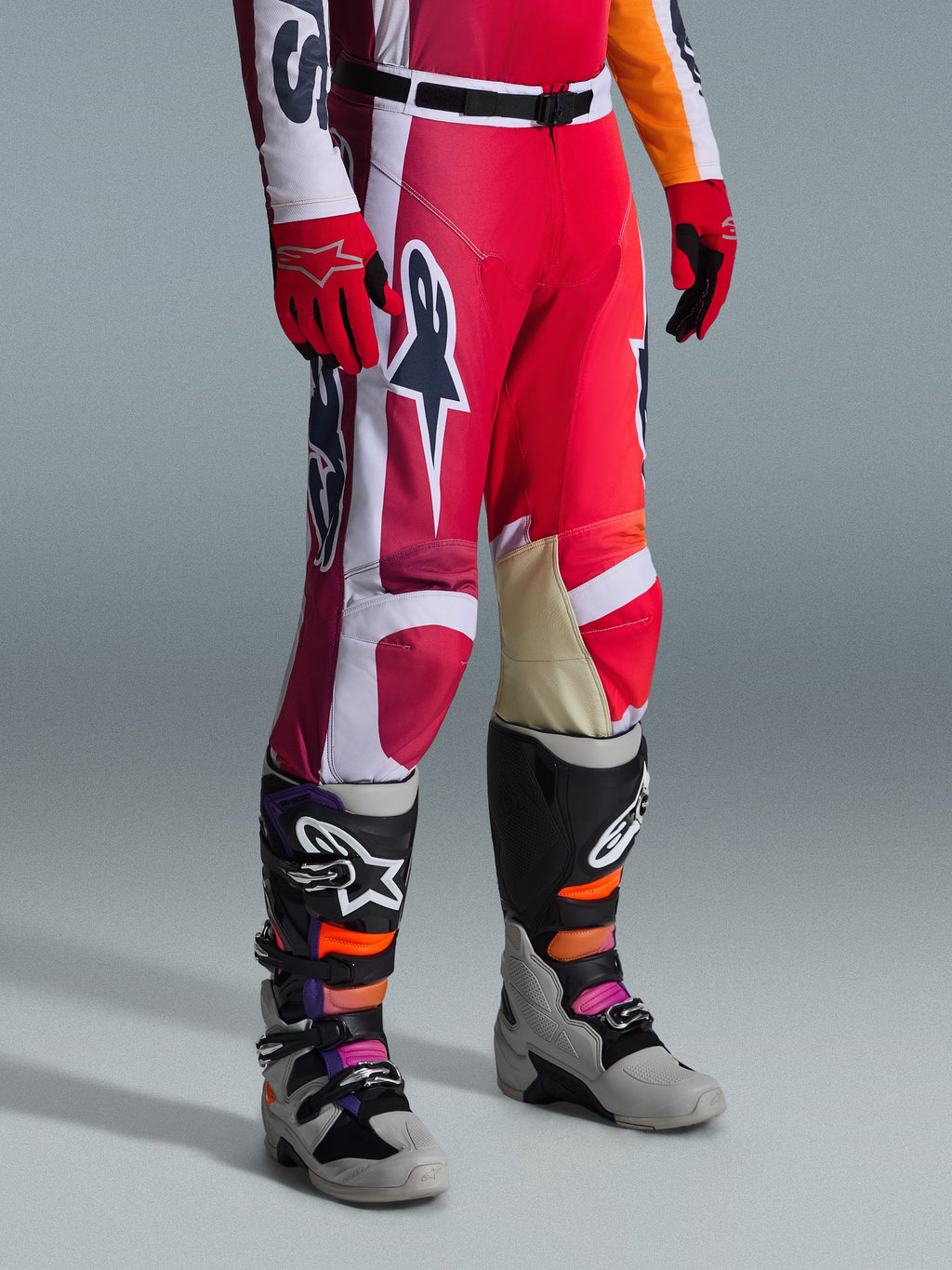 Alpinestars 2026 Racer Portl Pants, calças de motocross, vermelhas, cinzento claro e cinzento escuro, usadas com luvas vermelhas a condizer e botas de motocross multicoloridas, com logótipos Alpinestars em destaque e painéis reforçados para corridas de off-road