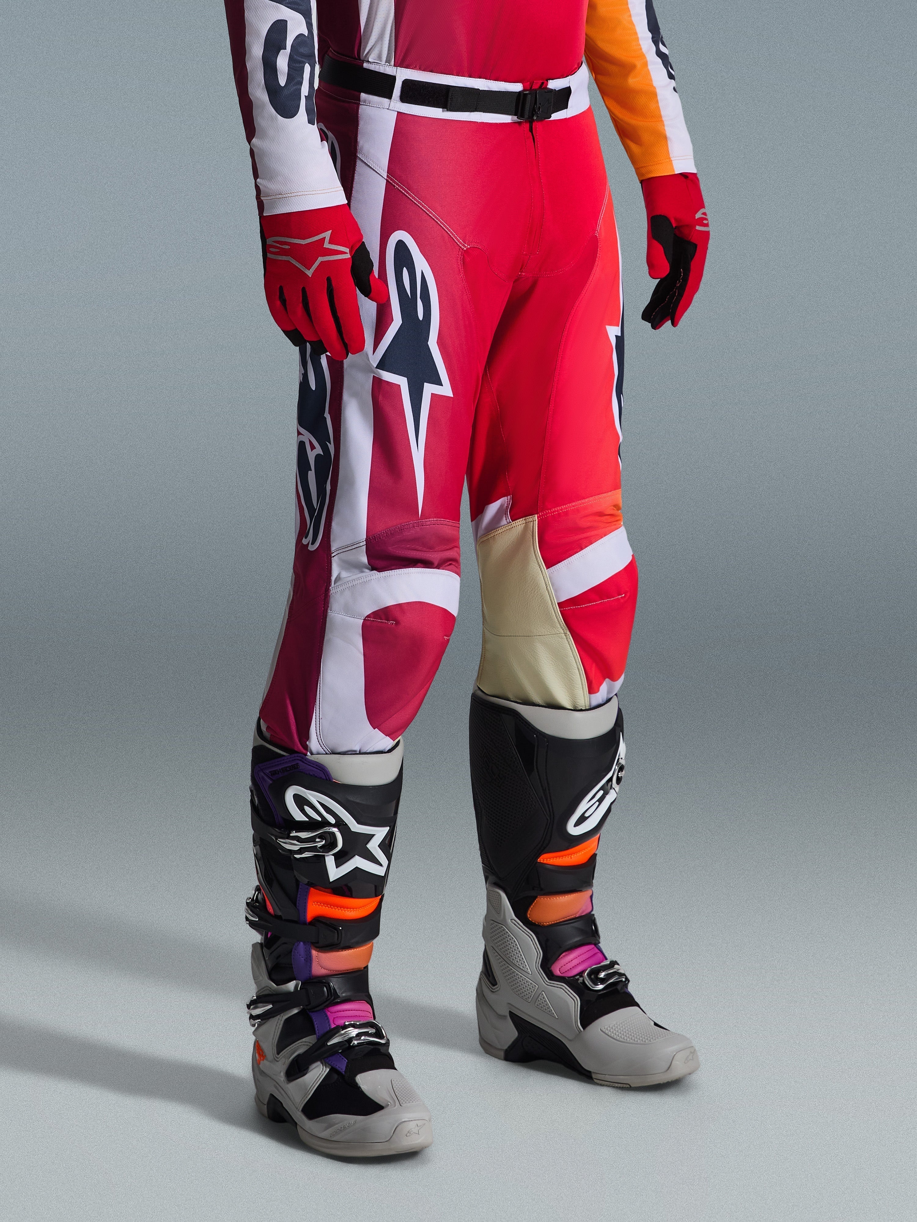 Alpinestars 2026 Racer Portl Pants, calças de motocross, vermelhas, cinzento claro e cinzento escuro, usadas com luvas vermelhas a condizer e botas de motocross multicoloridas, com logótipos Alpinestars em destaque e painéis reforçados para corridas de off-road