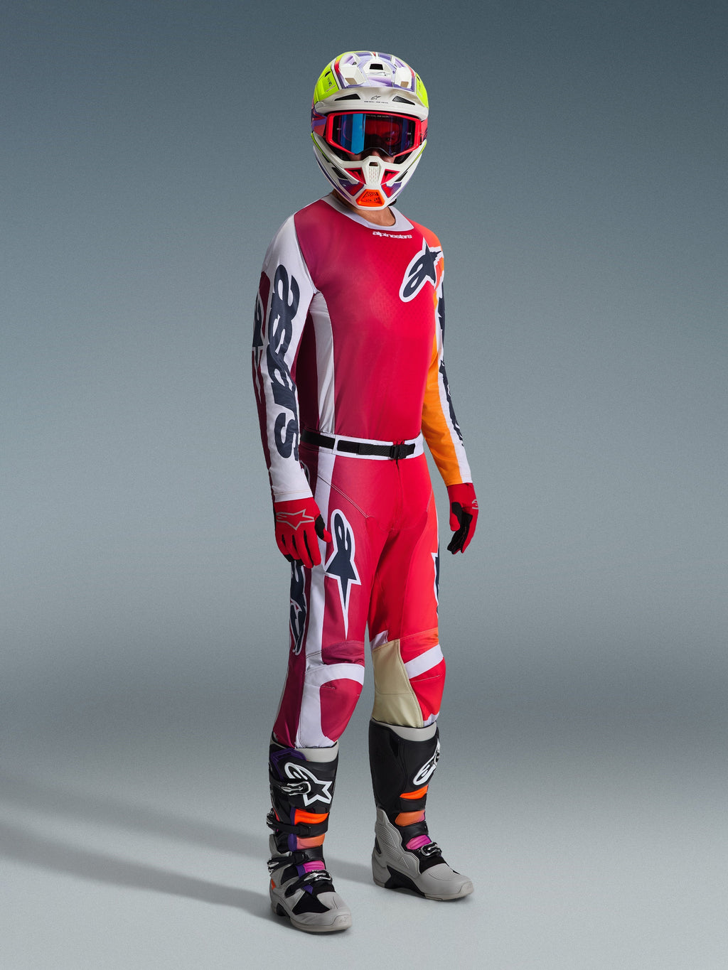 Alpinestars 2026 Racer Portl Pants, calças de motocross, vermelho, cinzento claro e cinzento escuro, usadas como parte de um conjunto de equipamento de corrida completo com camisola a condizer, luvas vermelhas, capacete colorido com óculos azuis e botas cinzentas, construção durável para desempenho em motocross off-road