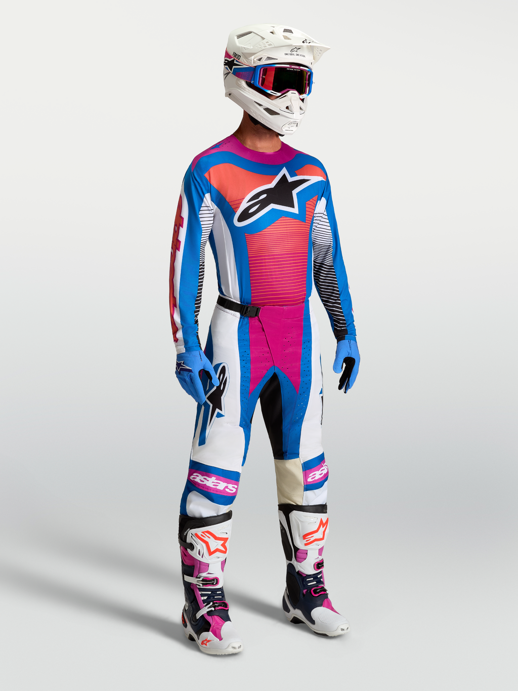 Calças Techstar Maven da Alpinestars em branco, coral e azul, mostradas em modelo num conjunto completo de motocross.