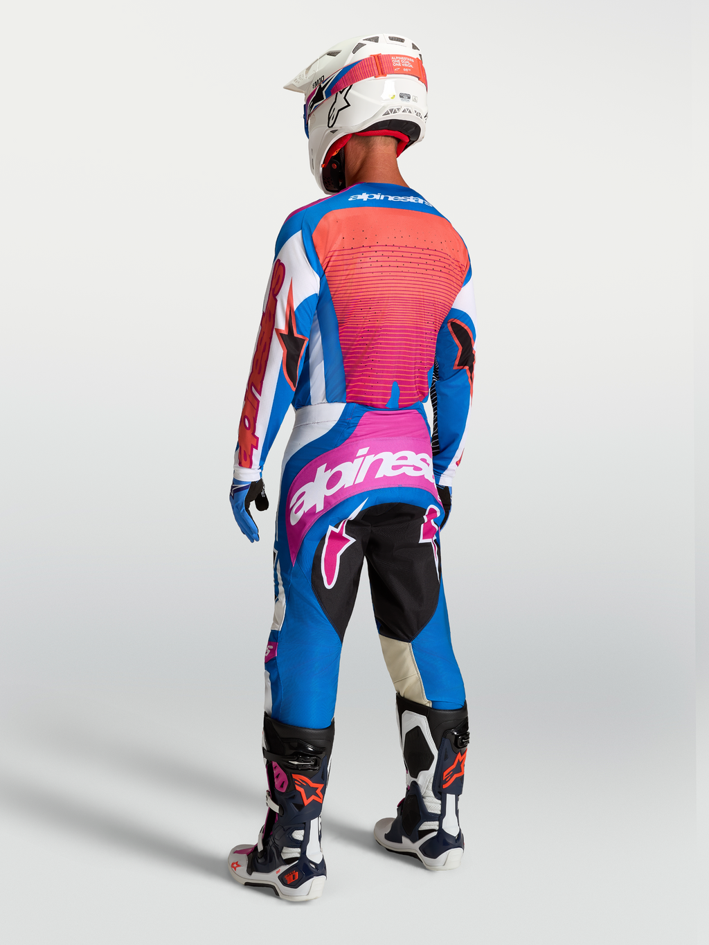 Alpinestars Calças Techstar Maven, calças de motocross para homem, azul e coral, vista traseira de piloto com equipamento de todo-o-terreno, ajuste de corrida ergonómico e logótipo Alpinestars.