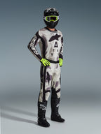 Alpinestars 2026 Racer Lahnd Gear Set, piloto de motocross com equipamento de corrida completo em Sand Camo e cinzento, camisola e calças a condizer com detalhes pretos e logótipos destacados, óculos e luvas em amarelo néon, capacete preto e botas pretas.