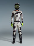 Piloto de motocross a usar o Alpinestars 2026 Racer Lahnd Gear Set, fato com padrão camuflado Sand Camo com design em branco, cinzento e preto, capacete preto com óculos verde néon, luvas verde néon vibrantes e botas pretas com logótipos brancos, equipamento completo coordenado para corridas todo-o-terreno