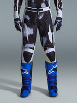Alpinestars 2026 Racer Lahnd Pants, calças de motocross, Iron Camo, usadas com luvas camufladas a combinar e botas azul vibrante e roxas, com grafismos de estrelas brancas estilizadas num padrão camuflado escuro, fecho de fivela magnética técnica, equipamento profissional de corrida para todo-o-terreno