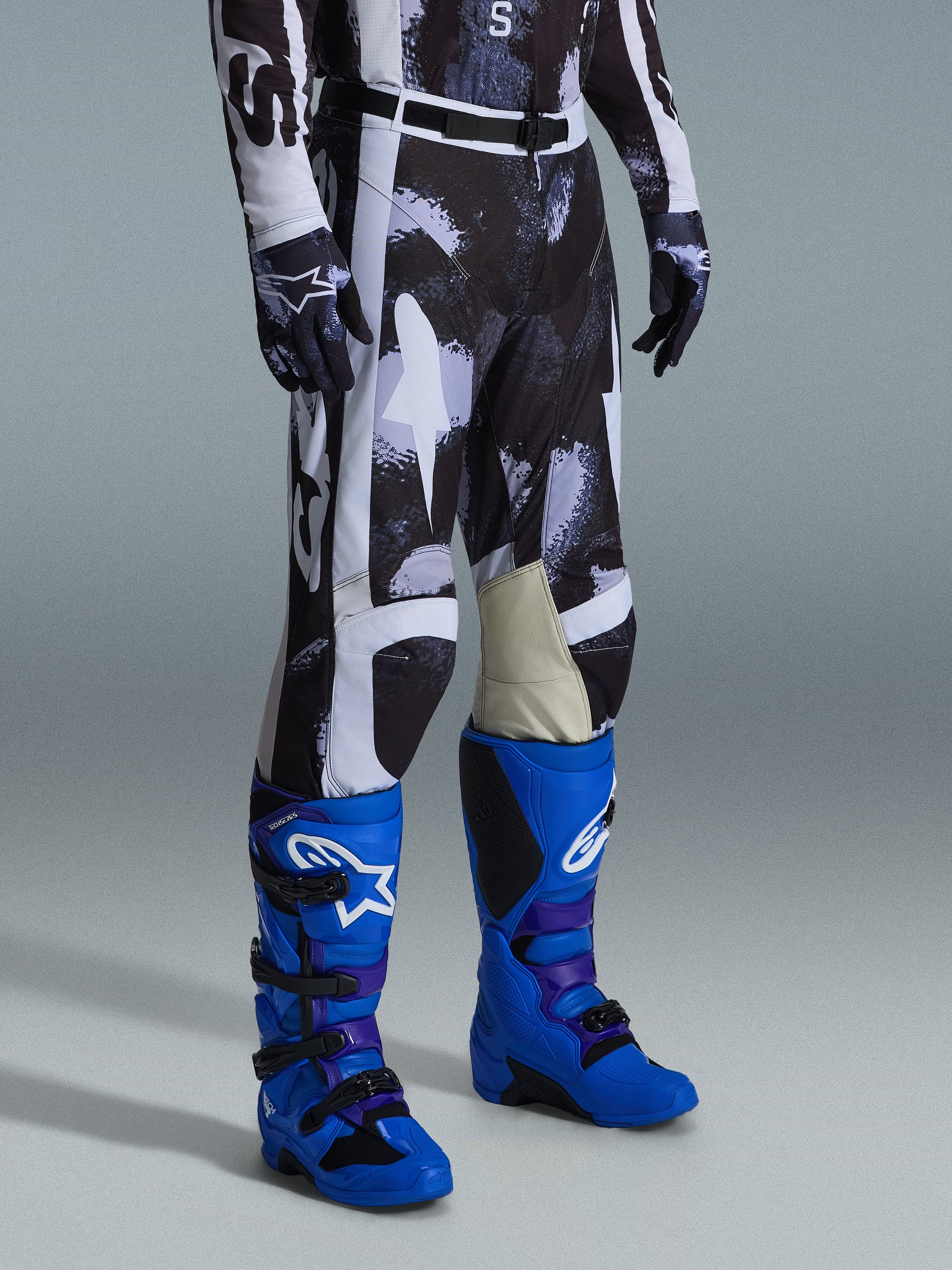 Alpinestars 2026 Racer Lahnd Pants, calças de motocross, padrão camuflado Iron Camo em cinzento e preto, usadas com botas de corrida azul brilhante e luvas a condizer, com painéis brancos e interior dos joelhos em couro de cabra, equipamento de alto desempenho para todo-o-terreno