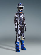 Piloto de motocross com equipamento completo Alpinestars, incluindo Calças Racer Lahnd 2026 com padrão Iron Camo e cinzento, camisola a condizer, botas de motocross azul brilhante e roxo, capacete azul e branco, equipamento de competição profissional para todo-o-terreno.