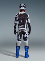 Alpinestars 2026 Racer Lahnd Pants, calças de motocross, padrão camuflado Iron Camo em cinzento e preto, vista traseira de piloto com equipamento de corrida completo com camisola a condizer e botas azuis, concebidas para desempenho off-road