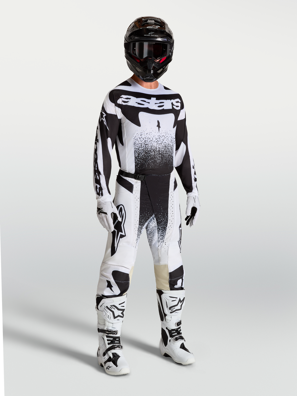 Calças Techstar Swan da Alpinestars, calças de motocross para homem, pretas e brancas, com ajuste atlético e tecido ripstop elástico, modelo vestido com equipamento de todo-o-terreno.