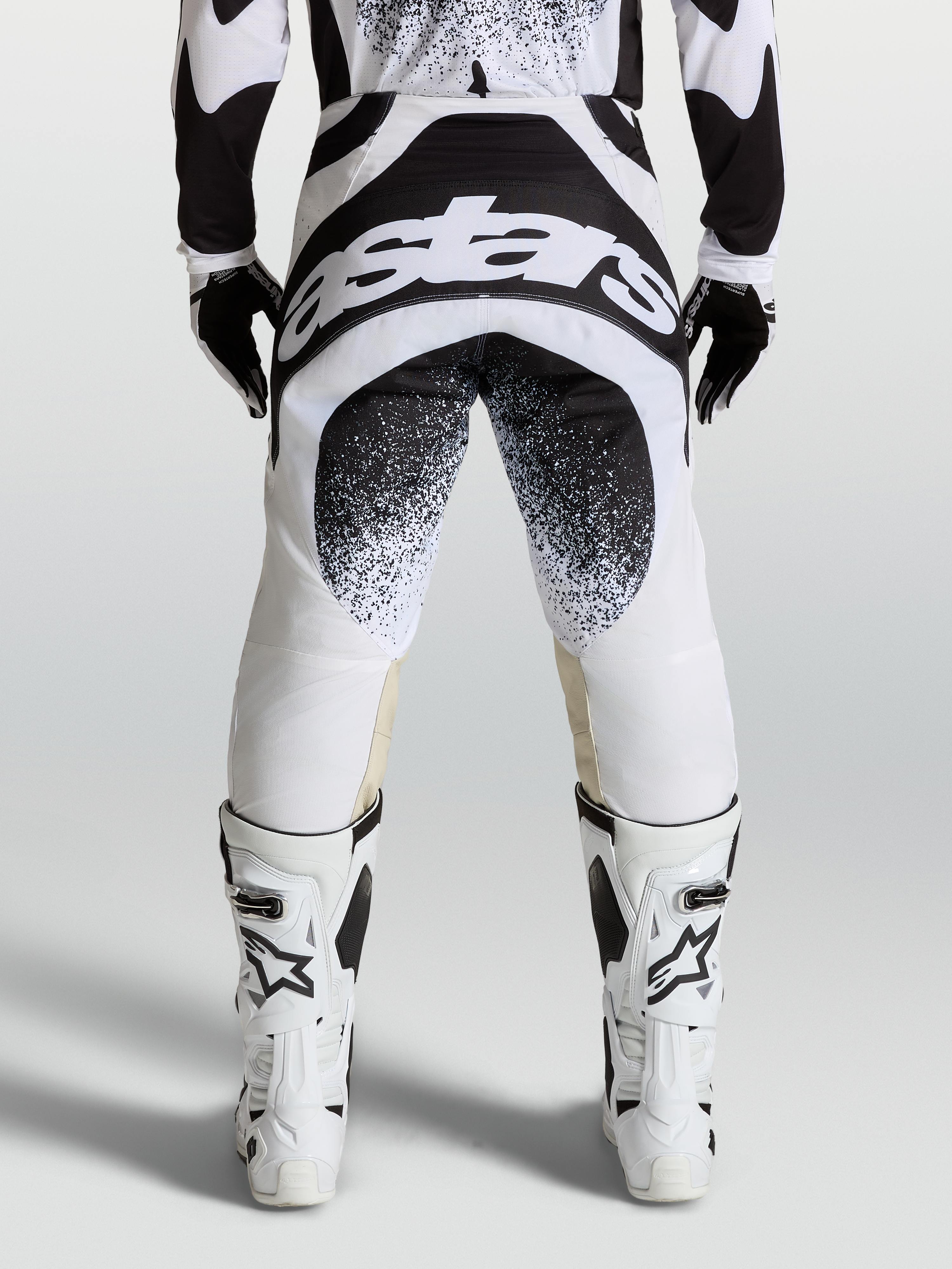 Alpinestars Calças Techstar Swan, calças de motocross profissionais, pretas e brancas, vista traseira com logótipo Astars, construção de joelho Babel.