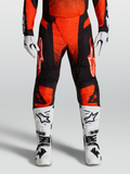 Alpinestars Calças Techstar Swan 2027, calças de motocross vermelhas e pretas, com botas e luvas de corrida brancas.