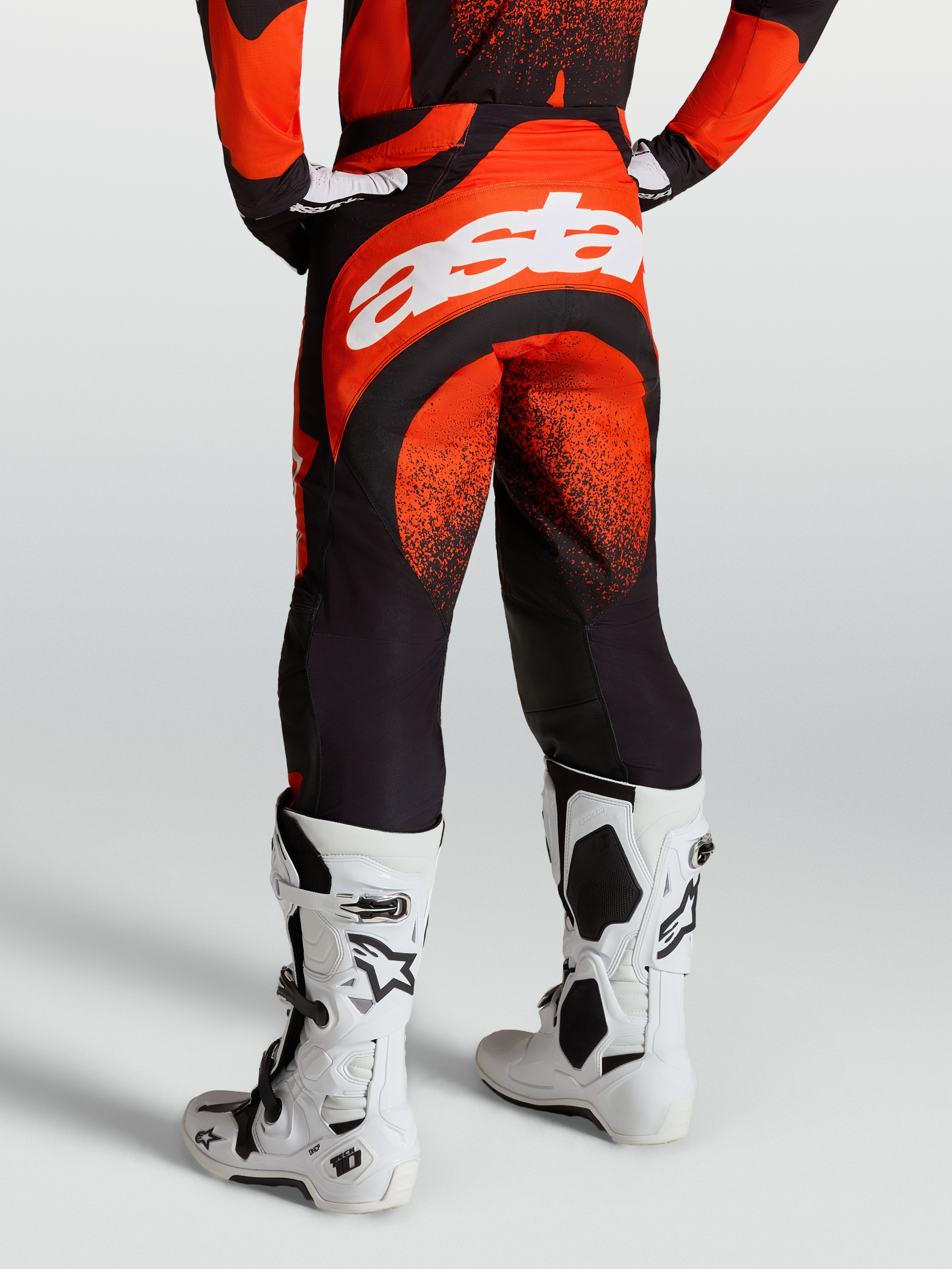 Alpinestars Calças Techstar Swan, calças de motocross para homem, vermelho cardinal e preto, logótipo Astar branco na traseira, exibidas com botas Tech 10 brancas.