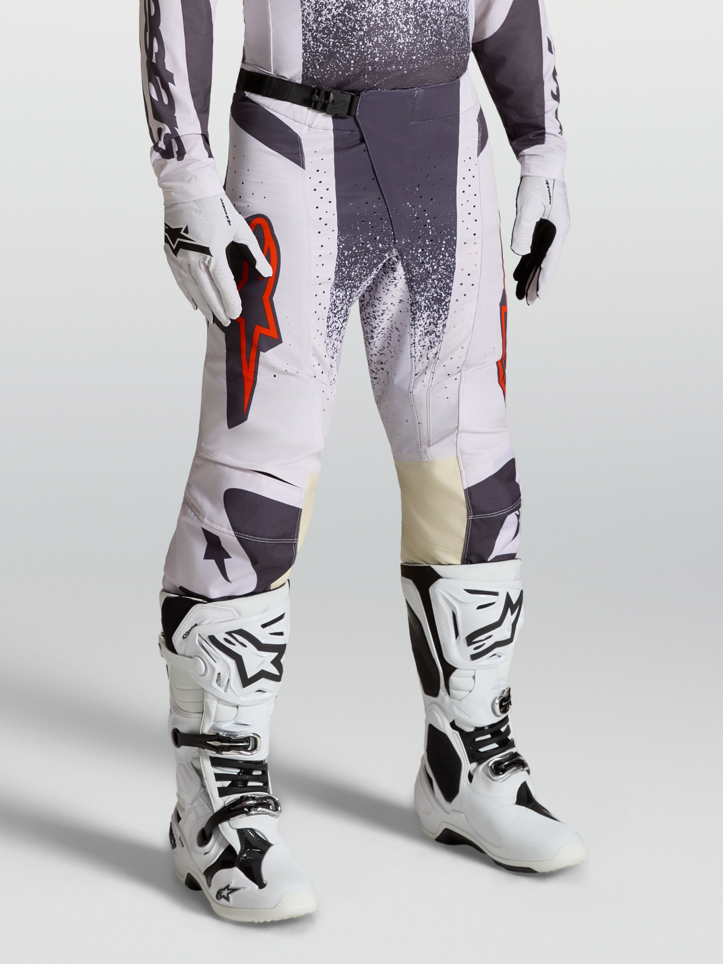 Calças Techstar Swan Alpinestars, calças de motocross para homem, lilás claro e cinzento escuro com detalhes em vermelho fluo, modelo equipado com luvas e botas.