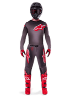 Motocross rider wearing complete Alpinestars 2025 Supertech Lipan gear set, Smoke Bright Red, featuring a dark grey jersey and pants with prominent red logos, black helmet with goggles, red and black gloves, and vibrant red motocross boots, coordinated professional racing outfit
