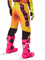 Alpinestars 2025 Supertech Lipan Gear Set, vista traseira de calças de motocross com gradiente amarelo e laranja e marca preta em destaque, combinadas com botas Tech 10 cor-de-rosa vivo e luvas amarelas, equipamento profissional de corrida todo-o-terreno