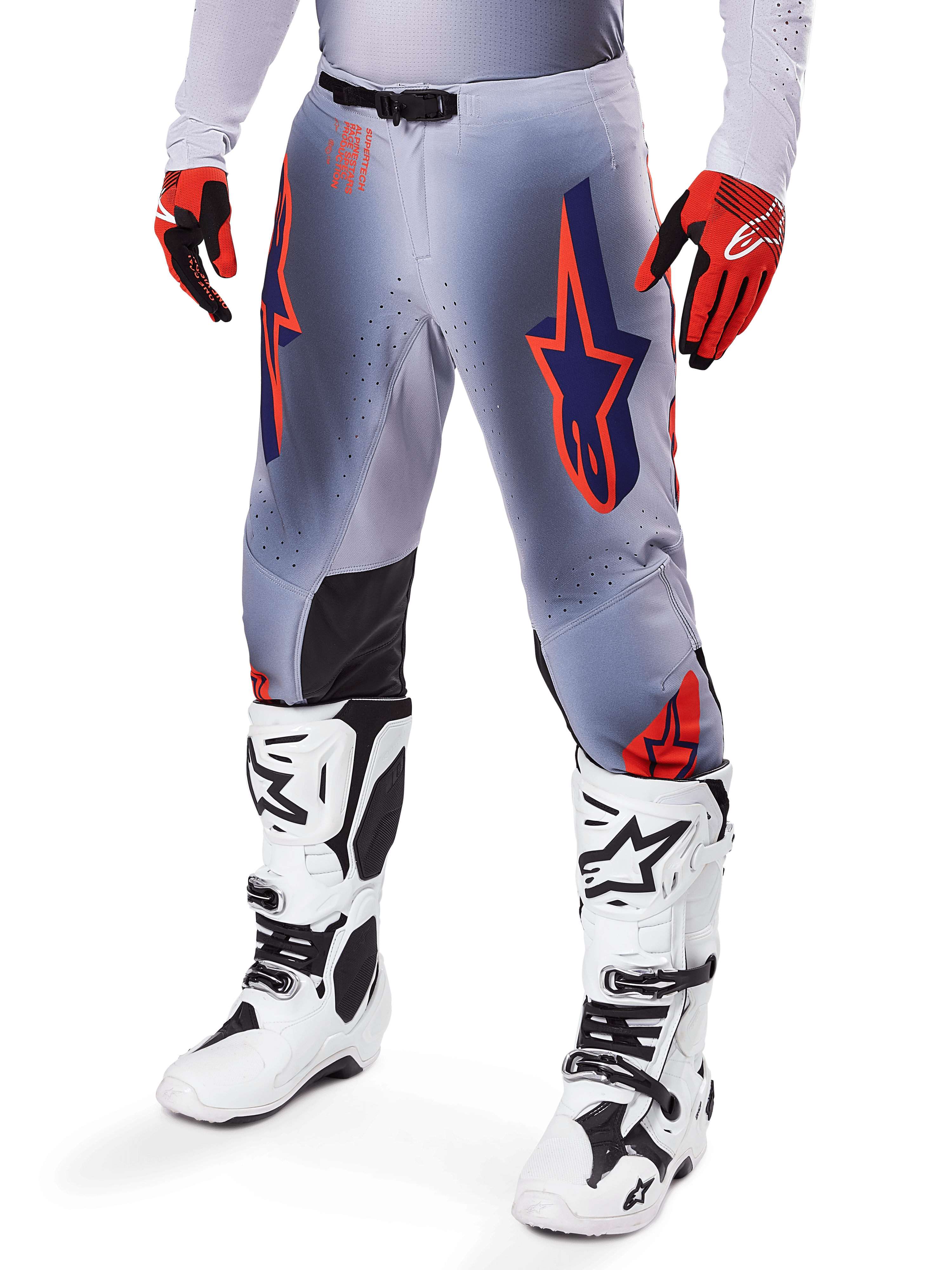 Alpinestars 2025 Supertech Lipan Pants, calças de motocross, cinzento e laranja fluo, com designs de estrelas azul-marinho e painéis internos pretos nos joelhos, usadas com luvas vermelho-alaranjadas e botas brancas, equipamento profissional de corrida todo-o-terreno