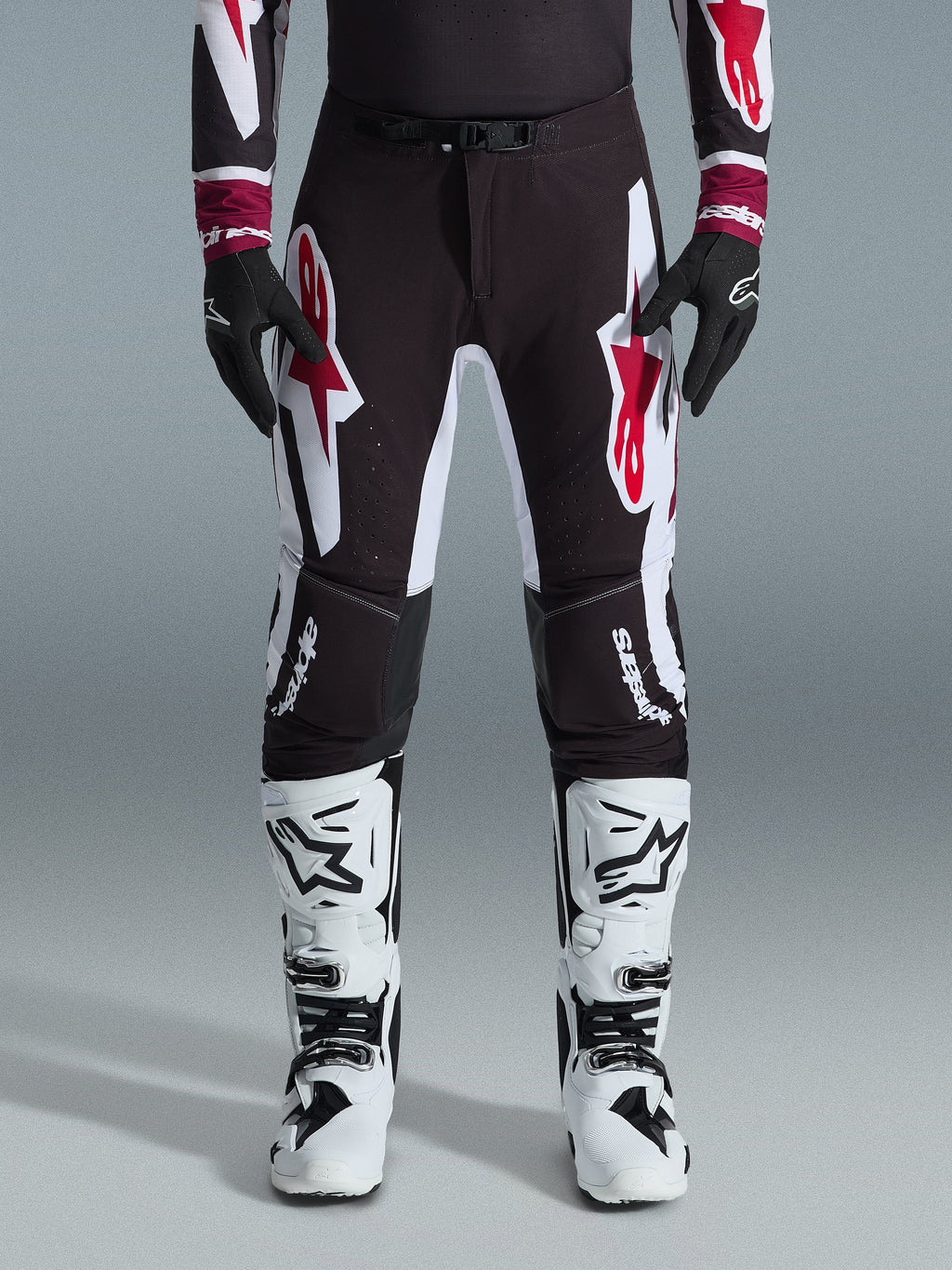 Alpinestars 2026 Supertech AFD Vista Pants, calças de motocross, pretas, vermelhas e brancas, com grandes logótipos gráficos nas coxas e joelhos, usadas com botas de competição brancas e luvas pretas, design desportivo de corrida para competição off-road de elite