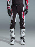 Alpinestars 2026 Supertech AFD Vista Pants, calças de motocross, pretas, vermelhas e brancas, com grandes logótipos gráficos nas coxas e joelhos, usadas com botas de competição brancas e luvas pretas, design desportivo de corrida para competição off-road de elite