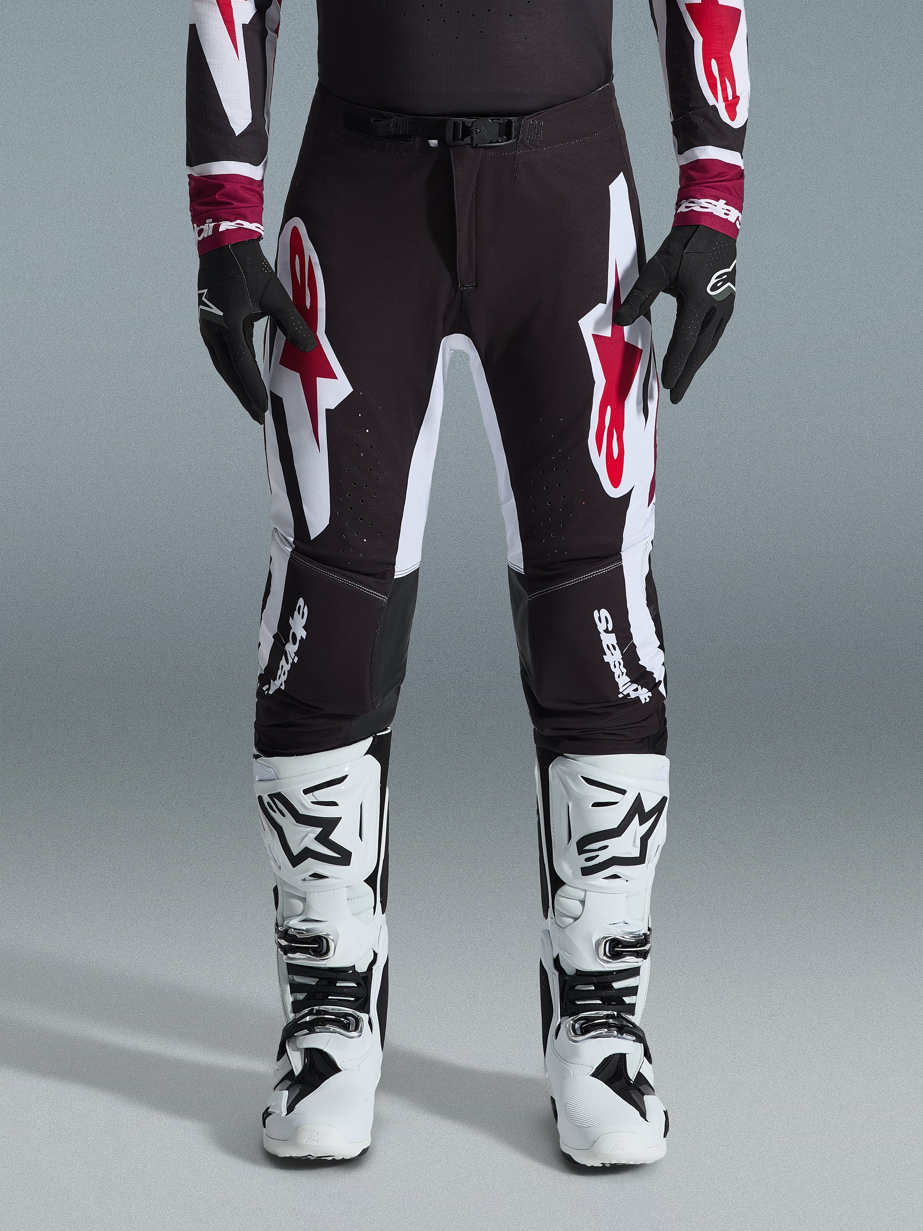 Alpinestars 2026 Supertech AFD Vista Pants, calças de motocross, pretas, vermelhas e brancas, com grandes logótipos gráficos nas coxas e joelhos, usadas com botas de competição brancas e luvas pretas, design desportivo de corrida para competição off-road de elite