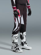 Alpinestars 2026 Supertech AFD Vista Pants, calças de motocross, pretas, vermelhas e brancas, usadas com botas de motocross brancas e pretas e luvas pretas, com padrões gráficos grandes em branco e vermelho e um design de ajuste atlético de competição