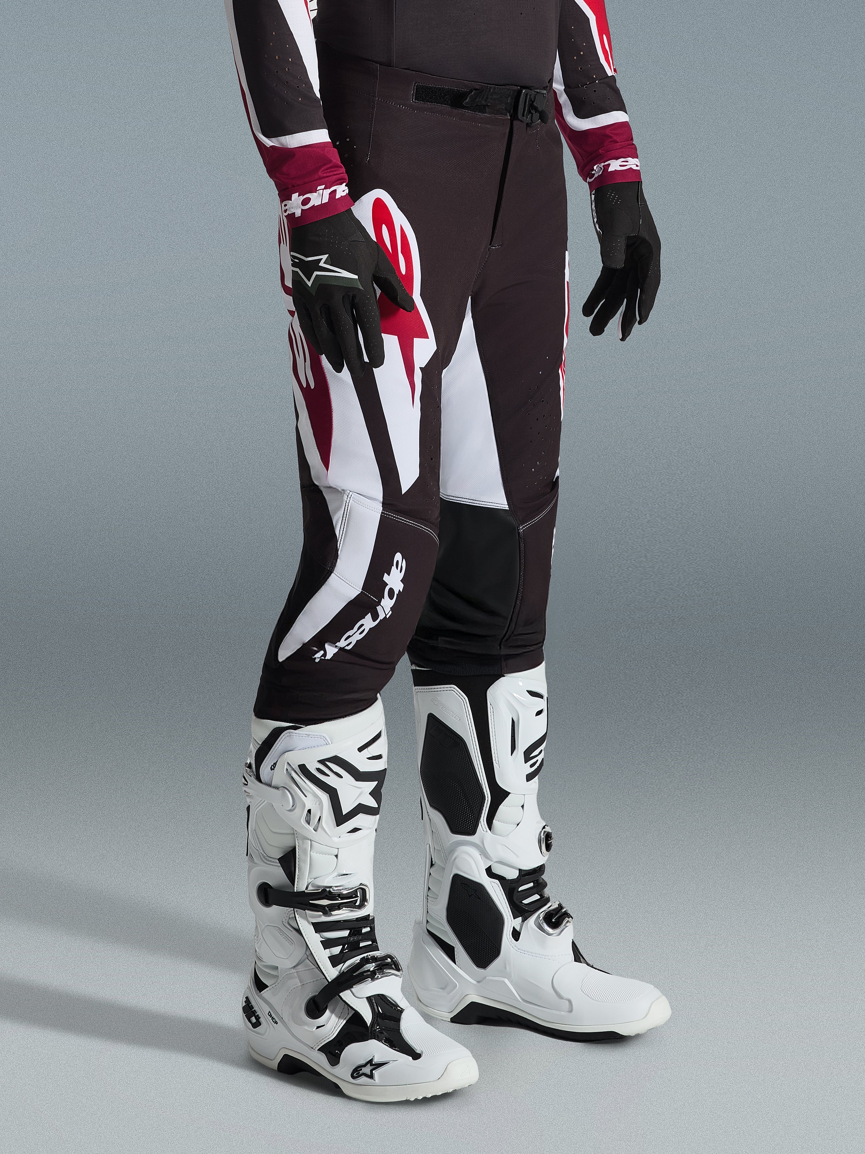 Alpinestars 2026 Supertech AFD Vista Pants, calças de motocross, pretas, vermelhas e brancas, usadas com botas de motocross brancas e pretas e luvas pretas, com padrões gráficos grandes em branco e vermelho e um design de ajuste atlético de competição