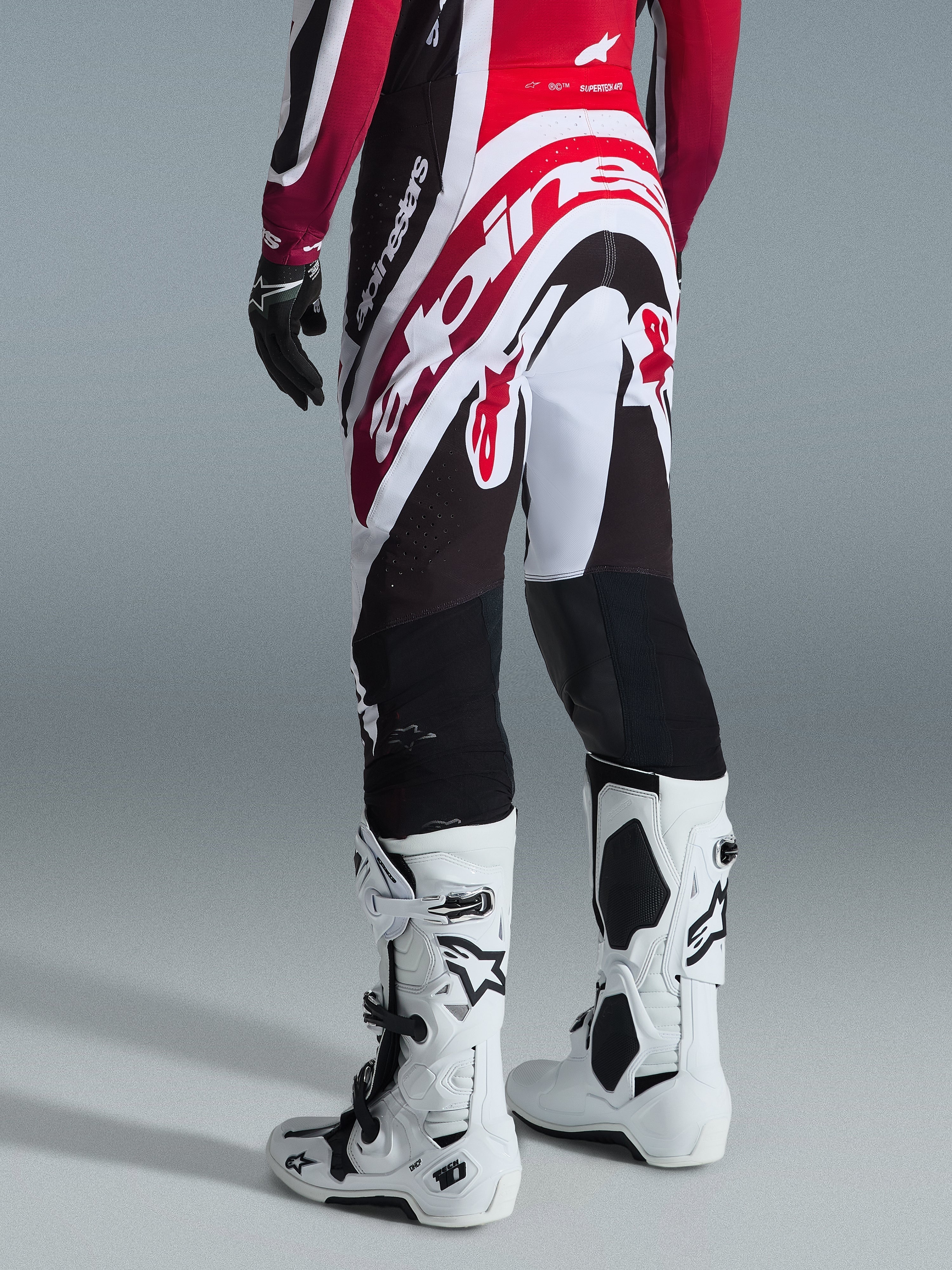 Calças Alpinestars 2026 Supertech AFD Vista, calças de motocross, pretas, vermelhas e brancas, vista traseira com grande logótipo Alpinestars no assento, combinadas com botas Tech 10 brancas e luvas pretas, design atlético para desempenho de elite em todo-o-terreno