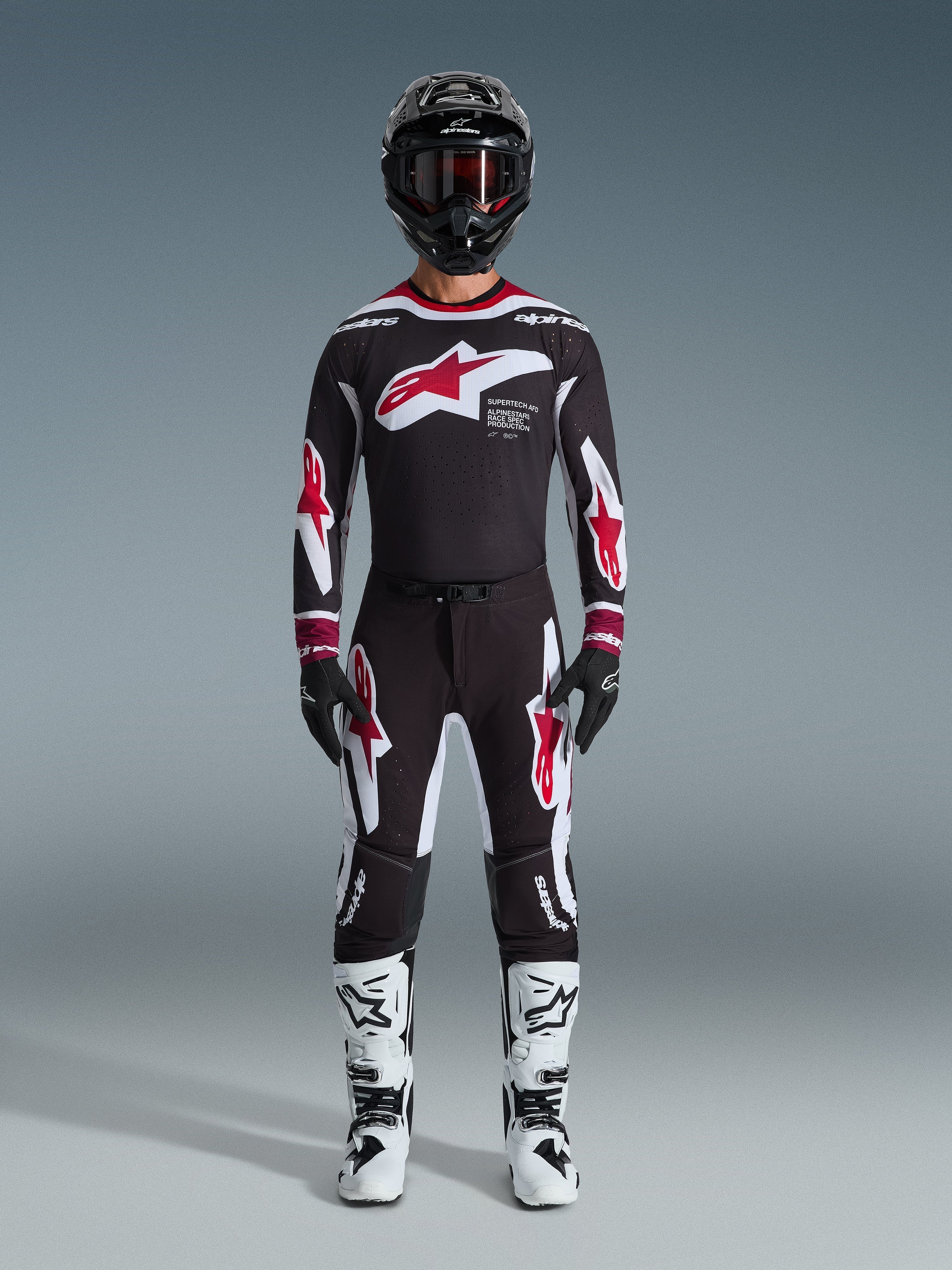 Calças Alpinestars 2026 Supertech AFD Vista, calças de motocross, pretas, vermelhas e brancas, usadas como um conjunto completo de equipamento de corrida com camisola a condizer, capacete preto e botas brancas, com logótipos Astars arrojados em vermelho e branco no peito e nas pernas, concebidas para um desempenho de elite em todo-o-terreno
