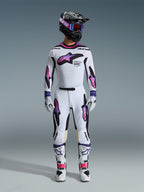 Piloto de motocross com um conjunto completo de equipamento de corrida, calças e camisola Alpinestars Supertech AFD Vista 2026 em branco, roxo e preto, luvas a condizer, botas brancas e pretas, capacete preto com óculos roxos, ajuste atlético para performance em todo-o-terreno