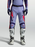 Alpinestars calças Racer Air Hunt, calças de motocross em violeta claro e roxo profundo com detalhes rosa fluorescente, design ventilado, usadas com botas brancas.