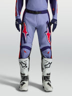 Alpinestars calças Racer Air Hunt, calças de motocross em violeta claro e roxo profundo com detalhes rosa fluorescente, design ventilado, usadas com botas brancas.