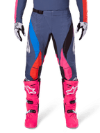 Alpinestars 2025 Techstar Dreem Pants, calças de motocross, cinzento multicolor com detalhes em azul, cor-de-rosa e laranja, usadas com botas cor-de-rosa vibrante e luvas brancas e pretas, com perfurações a laser nas coxas e fivela magnética na cintura, equipamento de ajuste atlético para competição todo-o-terreno