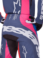 Alpinestars 2025 Techstar Dreem Pants, calças de motocross, cinza multicolor com detalhes em rosa e branco, detalhe da vista traseira com logótipo Alpinestars de grandes dimensões no assento e texto de especificações técnicas na cintura, usadas como parte de um conjunto de equipamento de corrida coordenado.