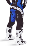Alpinestars 2025 Techstar Dreem Pants, calças de motocross, pretas e azuis, vista traseira com logótipo Alpinestars em destaque a branco no assento, usadas com botas de motocross brancas e pretas e camisola azul a combinar, corte atlético para corridas todo-o-terreno