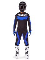 Piloto de motocross a usar o Conjunto de Equipamento Alpinestars Techstar Dreem 2025, camisola preta com painel frontal e mangas azuis, calças pretas e azuis coordenadas, capacete preto com óculos e botas brancas, conjunto completo de motocross para corridas fora de estrada