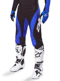 Alpinestars 2025 Techstar Dreem Pants, calças de motocross, pretas e azuis, usadas com botas de motocross brancas e luvas azuis, com o logótipo Alpinestars branco na perna, construção durável para corridas de todo-o-terreno