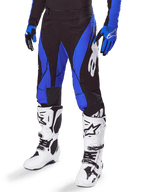 Alpinestars 2025 Techstar Dreem Pants, calças de motocross, pretas e azuis, usadas com botas de motocross brancas e luvas azuis, com o logótipo Alpinestars branco na perna, construção durável para corridas de todo-o-terreno