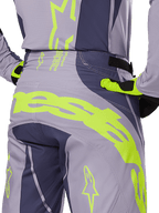 Alpinestars 2025 Techstar Dreem Pants, calças de motocross, cinzento e cinzento escuro com detalhes em amarelo néon, vista traseira com logótipo Alpinestars em destaque na zona da pala, usadas com camisola e luvas a combinar, concebidas para corridas todo-o-terreno.