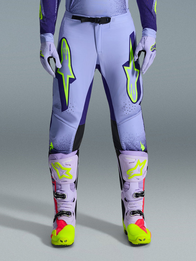 Alpinestars 2026 Supertech Scenz Pants, Motocross Pants, Purple Yellow Fluo, featuring large neon yellow logos on the thighs, worn with matching purple and yellow motocross boots and gloves, athletic-fit performance design for off-road racing