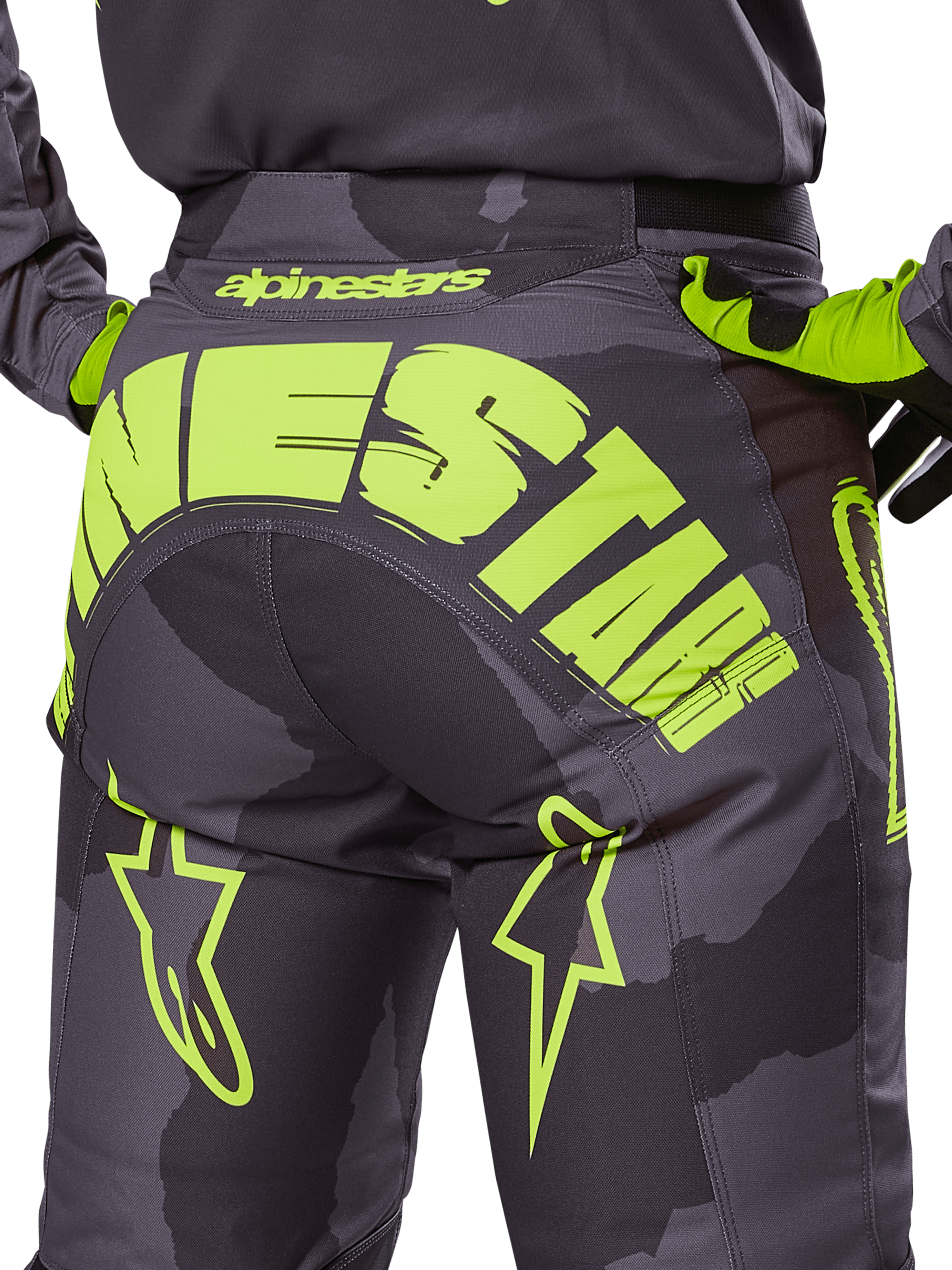 Alpinestars 2025 Racer Hollow Pants, calças de motocross, camuflagem escura e amarelo néon, com um grande logótipo Alpinestars amarelo na parte traseira, padrão de camuflagem tática com detalhes amarelos vibrantes e construção durável para corridas todo-o-terreno.