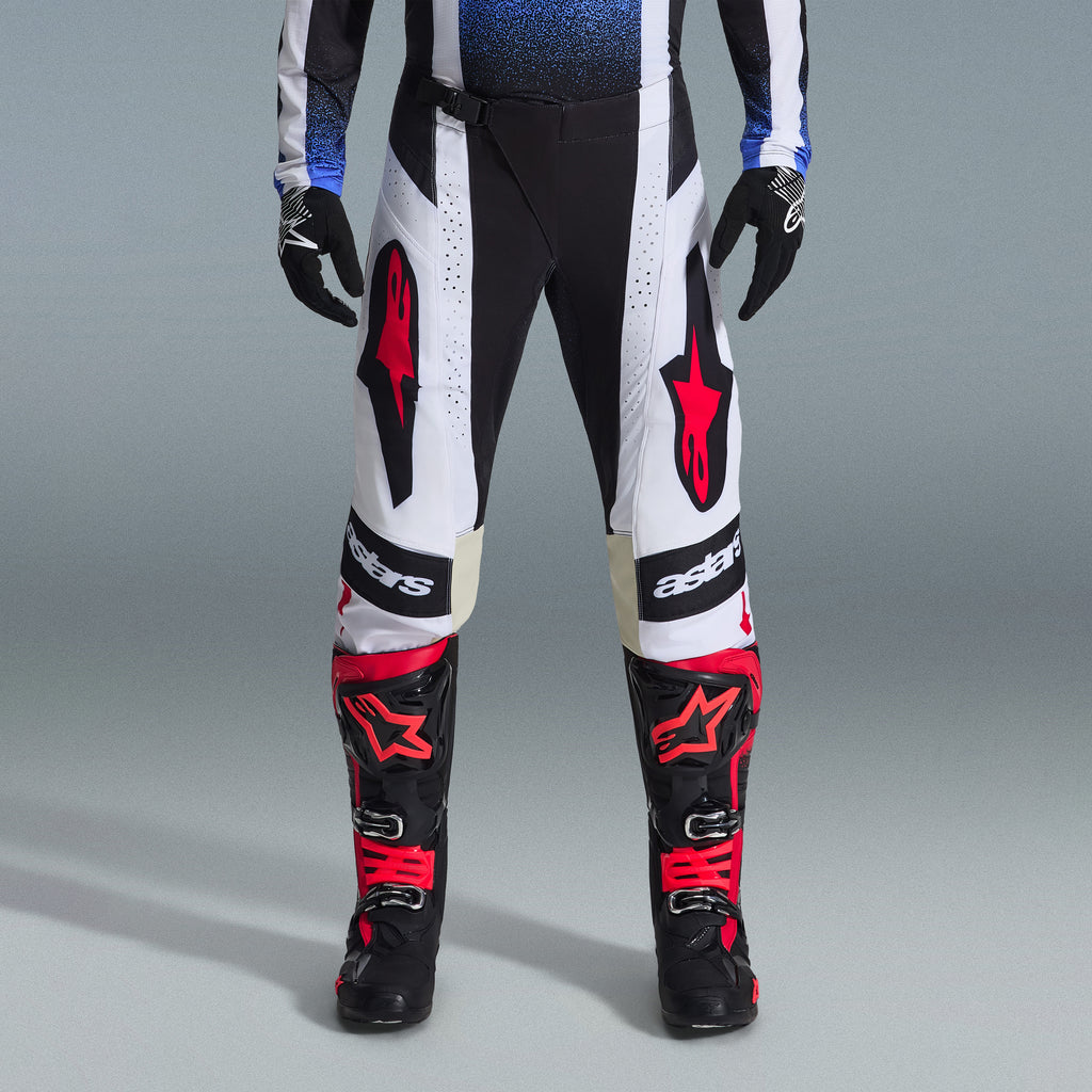 Conjunto de Equipamento Alpinestars Techstar Knif 2026, equipamento de motocross, calças pretas e brancas com grandes logótipos de estrela vermelhos, usadas com botas de corrida pretas e vermelhas e luvas pretas, corte atlético profissional para desempenho em todo-o-terreno