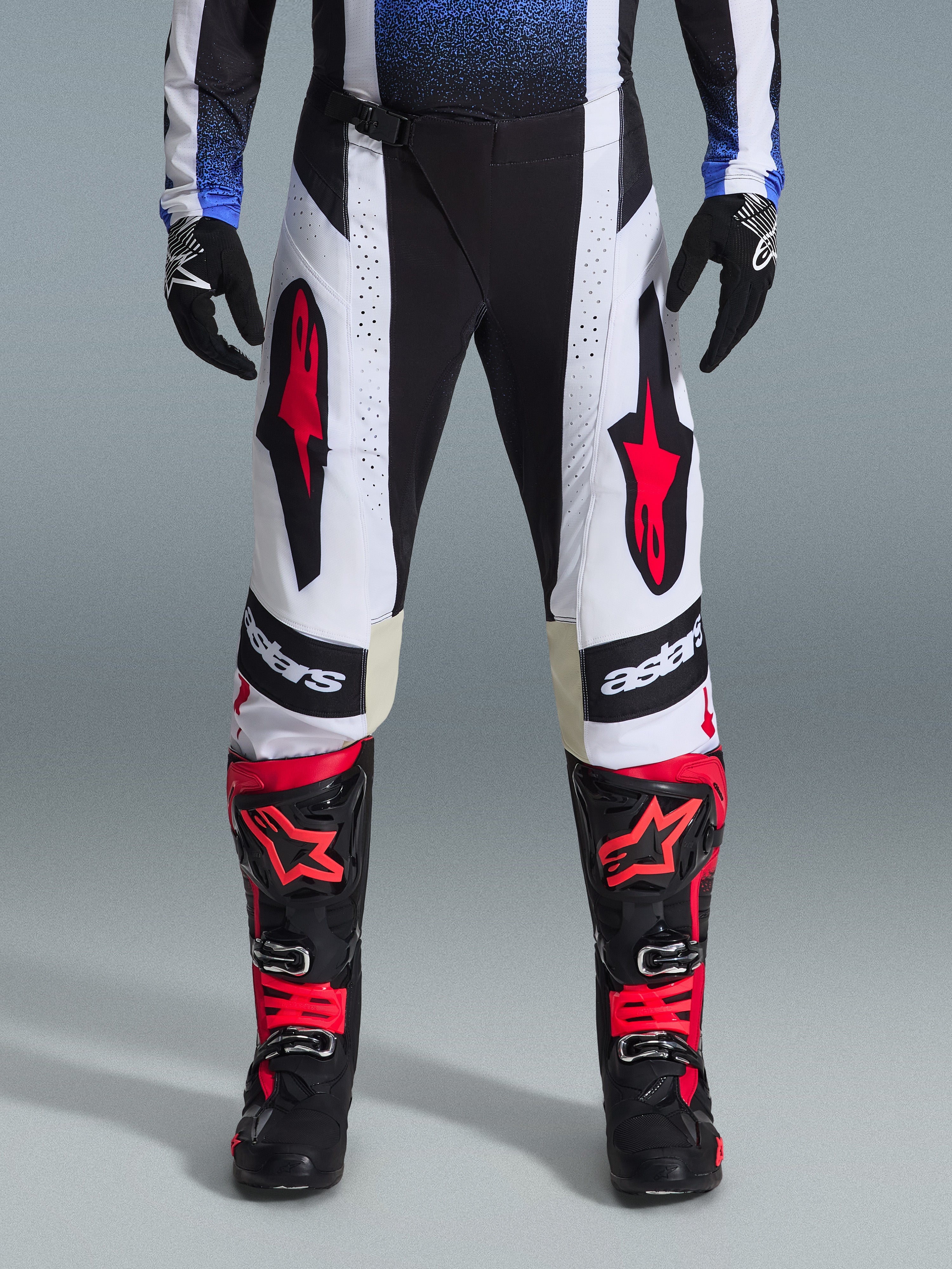 Alpinestars 2026 Techstar Knif Pants, calças de motocross, pretas, brancas e vermelhas, usadas com botas vermelhas e pretas a condizer e luvas pretas, com logótipos de estrela vermelha proeminentes em painéis brancos e detalhes técnicos perfurados para todo-o-terreno