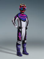 Piloto de motocross com o conjunto de equipamento Alpinestars 2026 Techstar Knif, camisola branca com detalhes em preto, azul e rosa, calças a condizer com logótipos Astars cor-de-rosa, capacete multicolorido com óculos, botas de corrida roxas, equipamento de alto desempenho coordenado para competição de motocross